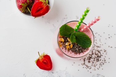 Pembe çilek, muz smoothie granola ve chia tohumu hafif beyaz beton zemin üzerine cam ile. Üstten görünüm. Kopya alanı.