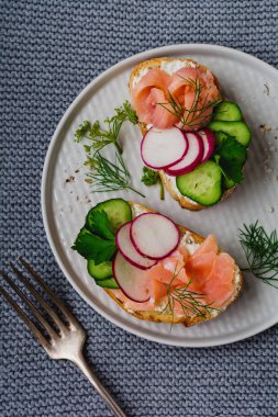 Pembe somon füme, turp, salatalık ve gri Seramik plaka ve tekstil zemin üzerine krem peynir sandviç. Geleneksel İskandinav tost. Üstten görünüm.