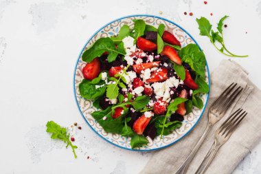 Pancar, çilek, seramik plaka eski beton tablo arka plan üzerinde beyaz peynir ve roka salatası. Üstten görünüm.