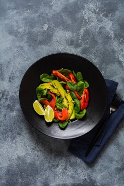 Avokado, somon, ıspanak, domates, çam fıstığı ve siyah susam salata siyah bir seramik tabak içinde. Üstten görünüm.