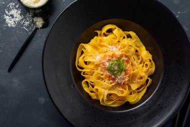Fettuccine makarna ile geleneksel İtalyan Passat sos ve parmesan peynir koyu arka plan üzerinde siyah plaka. Üstten görünüm.