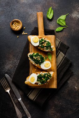 Fried ıspanak, yumurta ve çam fıstığı sandviç kahverengi vintage eski concretebackground üzerinde. Lezzetli sağlıklı kahvaltı veya aperatif. Üstten görünüm.