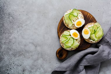 Gri beton zemin üzerine salatalık, yumurta ve lor peynirli sandviç. Üstten görünüm.