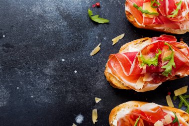 Jamon, roka ve beton eski koyu arka plan üzerinde sert peynir ile açık sandviçler. Rustik tarzı. Üstten Görünüm.