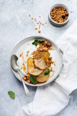 Gri seramik tabakta sağlıklı bir kahvaltı için karamelize armut, granola, fındık ve eritilmiş şeker içeren Yunan yoğurdu. Kırsal tarzda. Üst görünüm.