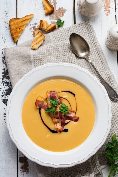 Potato soup cream with bacon and soy sauce in white bowl, on light old wooden background. Top view.