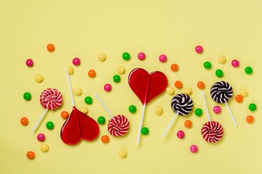 Açık sarı arka plan üzerinde renkli şekerler ve lolipoplar. Kopyalama alanı ile üstte görünüm.