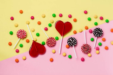 Açık sarı arka plan üzerinde renkli şekerler ve lolipoplar. Kopyalama alanı ile üstte görünüm.