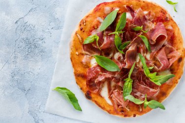Jamonlu ev yapımı pizza, mozzarella ve arka planda taze fesleğen yaprakları. Üst görünüm.
