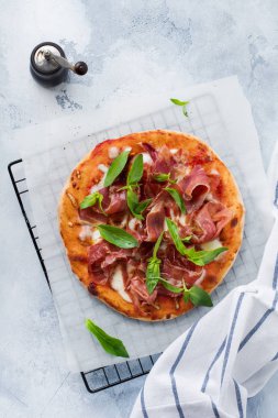 Jamonlu ev yapımı pizza, mozzarella ve arka planda taze fesleğen yaprakları. Üst görünüm.