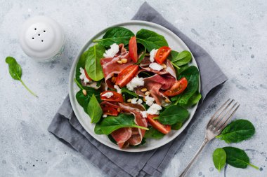 Eski bir beton gri arka plan üzerinde basit bir seramik plaka içinde ıspanak, kiraz domates, mozzarella, çam fıstığı ve zeytinyağı ile jambon ile Bahar Salatası.