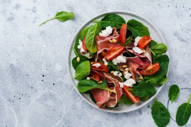 Eski bir beton gri arka plan üzerinde basit bir seramik plaka içinde ıspanak, kiraz domates, mozzarella, çam fıstığı ve zeytinyağı ile jambon ile Bahar Salatası.