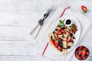 Beyaz tabakta çikolata tepesi ve taze çilek ile lezzetli krep, üst görünümü.