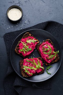 Bruschetta karanlık beton zemin üzerine kırmızı pancar Humus, roka ve susam tohumu ile. Üstten görünüm.
