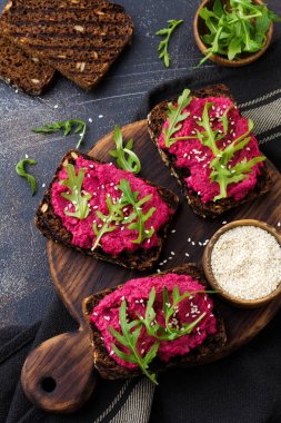 Bruschetta karanlık beton zemin üzerine kırmızı pancar Humus, roka ve susam tohumu ile. Üstten görünüm.