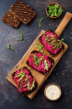 Bruschetta karanlık beton zemin üzerine kırmızı pancar Humus, roka ve susam tohumu ile. Üstten görünüm.