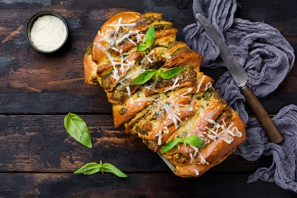 Pull-apart bread with Italian pasta pesto, basil and parmesan cheese in baking form over old wooden background. Top view. Rustic stile.