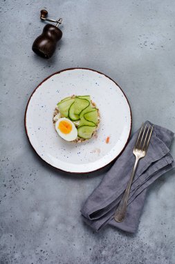 Gri eski arka plan üzerinde seramik plaka üzerinde haşlanmış yumurta ve salatalık ile Sandviç. Üstte görüntü.