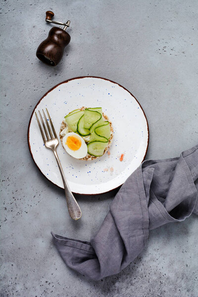 Sandwich with boiled egg and cucumber on ceramic plate on gray old background. Top view.