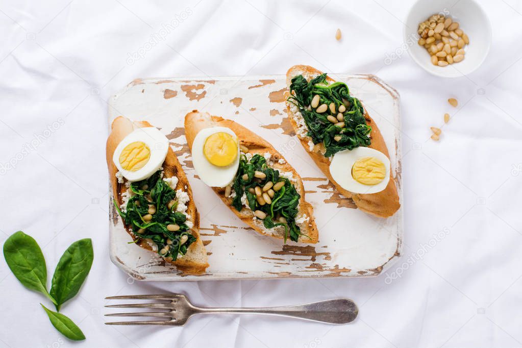 Fried spinach, egg and pine nuts sandwiches or bruschetta on light background. Delicious healthy breakfast or snack. Top view.