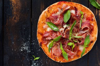 Jamon, mozzarella ve taze fesleğen yaprakları ile ev yapımı pizza eski bir ahşap arka plan üzerinde. Üstte görüntü.