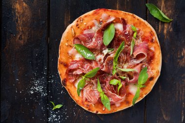 Jamon, mozzarella ve taze fesleğen yaprakları ile ev yapımı pizza eski bir ahşap arka plan üzerinde. Üstte görüntü.