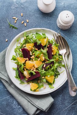 Pancar, portakal, çam fındık, zeytin yağı, seramik plaka eski beton tablo arka plan üzerinde beyaz peynir ve roka salatası. Üstten görünüm.