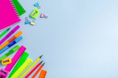 Defter, renkli kalemler, cetvel, kalem, silgi, keskinleştirme ve daha fazlası. Mavi arka planda okul ve ofis kırtasiye. Kavram okula geri döndü. Üstte görüntü.