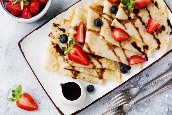 Delicious crepe with chocolate topping and fresh strawberry on white plate, top view.