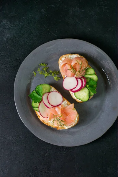 Gri seramik plaka ve tekstil arka plan üzerinde füme pembe somon, turp, salatalık ve krem peynir ile Sandviçler. Geleneksel İskandinav tostu. Üst te. Kare görüntü