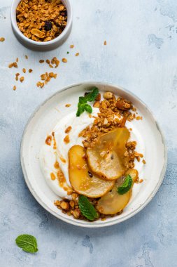 Gri seramik tabakta sağlıklı bir kahvaltı için karamelize armut, granola, fındık ve eritilmiş şeker içeren Yunan yoğurdu. Kırsal tarzda. Üst görünüm.