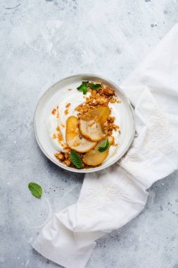 Gri seramik tabakta sağlıklı bir kahvaltı için karamelize armut, granola, fındık ve eritilmiş şeker içeren Yunan yoğurdu. Kırsal tarzda. Üst görünüm.