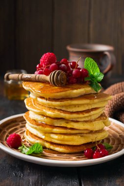 Eski bir ahşap arka plan üzerinde bal, taze ahududu ve kırmızı kuş üzümü ile ev yapımı küçük krep yığını. Seçici odaklama.