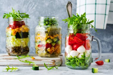 İtalyan roka salatası, mozzarella ve masada öğle yemeği için kavanozda servis edilen vişneli domates. Seçici odak.