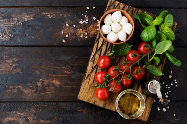 Taze kiraz domates, fesleğen yaprakları, mozzarella peyniri ve eski ahşap arka plan üzerinde zeytinyağı. Caprese salata malzemeleri. Seçici odaklama.
