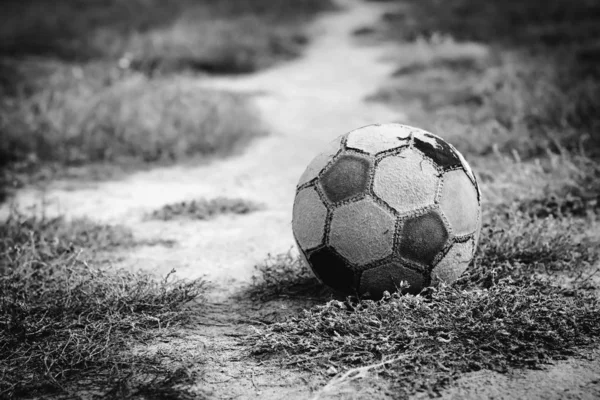 Old soccer ball lying on the grass for street football before the start of the game. Black and white image. Selective focus.