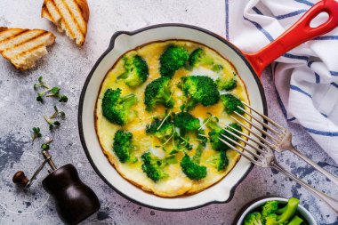 Brokolili omlet ve kırmızı soğanlı yeşil taze soğan eski gri beton arka planda demir tava. Üst görünüm.