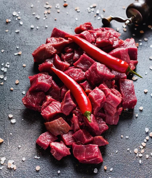 Cut beef into small pieces with sea salt, dried herbs and chili peppers on dark slate or concrete   background. Top view.