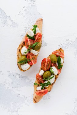 Beyaz tabak eski ışık arka plan üzerinde kiraz domates, mozzarella, zeytin ve fesleğen ile Caprese bruschetta tost. Üstte görüntü.