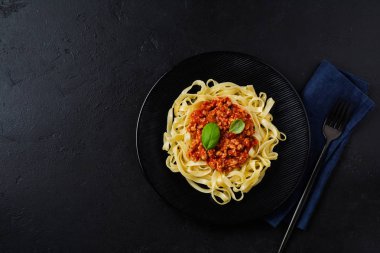 Geleneksel İtalyan yemeği fettuccine makarna, bolonez sosu, fesleğen ve parmesan peyniri ile koyu ahşap arka planda. Üst görünüm.