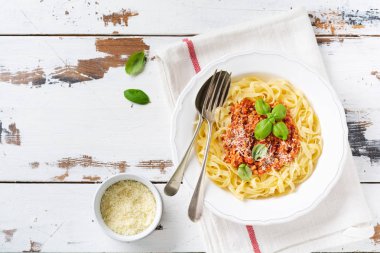 Hafif ahşap arka plan üzerinde beyaz bir tabakta bolonya sos, fesleğen ve parmesan peyniri ile geleneksel İtalyan çanak fettuccine makarna. Üstte görüntü.
