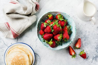 Eski seramik kasede taze çilek ve gri beton arka planda yeşil yapraklar. Sağlıklı kahvaltı konsepti. Üst görünüm.