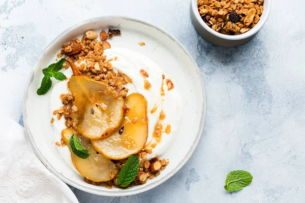 Greek yogurt with caramelized pear, granola, nuts and melted sugar for a wholesome breakfast on a gray ceramic plate. Rustic style. Top view. — Stock Image Greek Yogurt Caramelized Pear Granola Nuts Melted Sugar Wholesome Breakfast Stock Picture