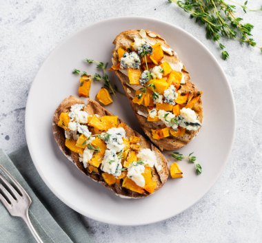 Fırınlanmış balkabağı sandviçi, mavi küflü Dorblu peynirli, bal ve kekik, beton, eski, aydınlık arka planda. Üst görünüm.
