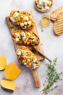 Fırınlanmış balkabağı sandviçi, mavi küflü Dorblu peynirli, bal ve kekik, beton, eski, aydınlık arka planda. Üst görünüm.