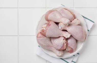 Çiğ tavuk bacağı, domates vişneli, otlu, fesleğenli ve baharatlı, beyaz mermer arka planda, uzay manzarasını kopyala. Sağlıklı beslenme öğle yemeği konsepti.