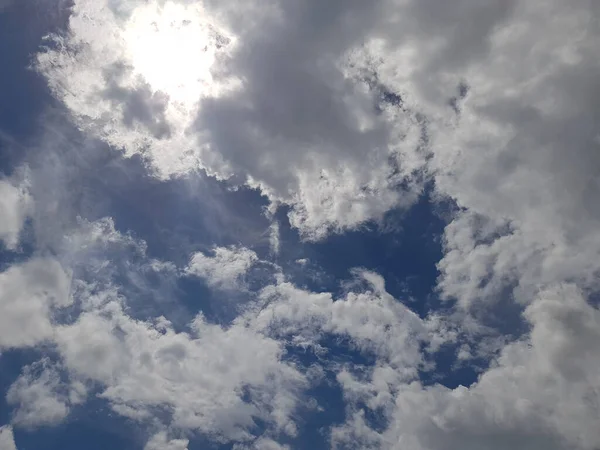 The bright sun in the blue sky covered with clouds.