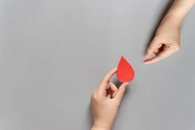 Kan bağışı. İnsan eli, gri arka plandaki bir ele kan damlası sembolü veriyor. Dünya kan bağışı günü ve hayat kurtarma konsepti. Düz yatıyordu. Boşluğu kopyala.