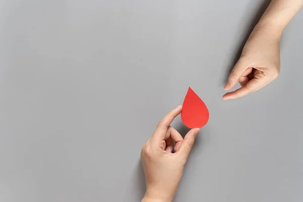 Kan bağışı. İnsan eli, gri arka plandaki bir ele kan damlası sembolü veriyor. Dünya kan bağışı günü ve hayat kurtarma konsepti. Düz yatıyordu. Boşluğu kopyala.