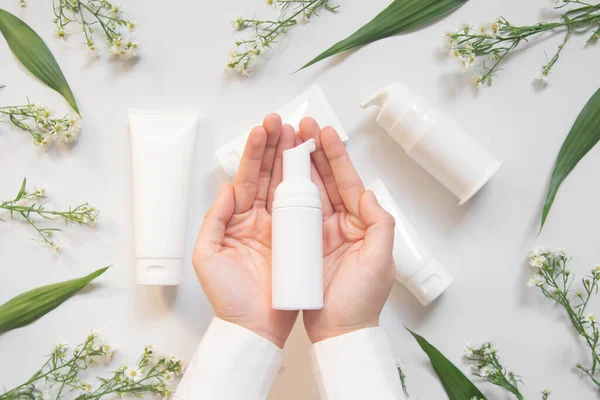 Güzellik doğal cilt bakım ürünleri geliştirme konsepti. Dermatolog elleri boş bir kozmetik şişeyle pompa dağıtıcısı ve beyaz arka planda organik malzeme tutuyor. Üst Manzara. Kapat..